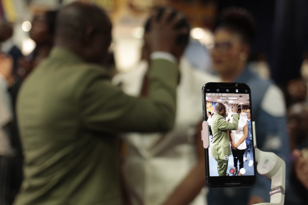 Pastor ministering and community member recording on mobile